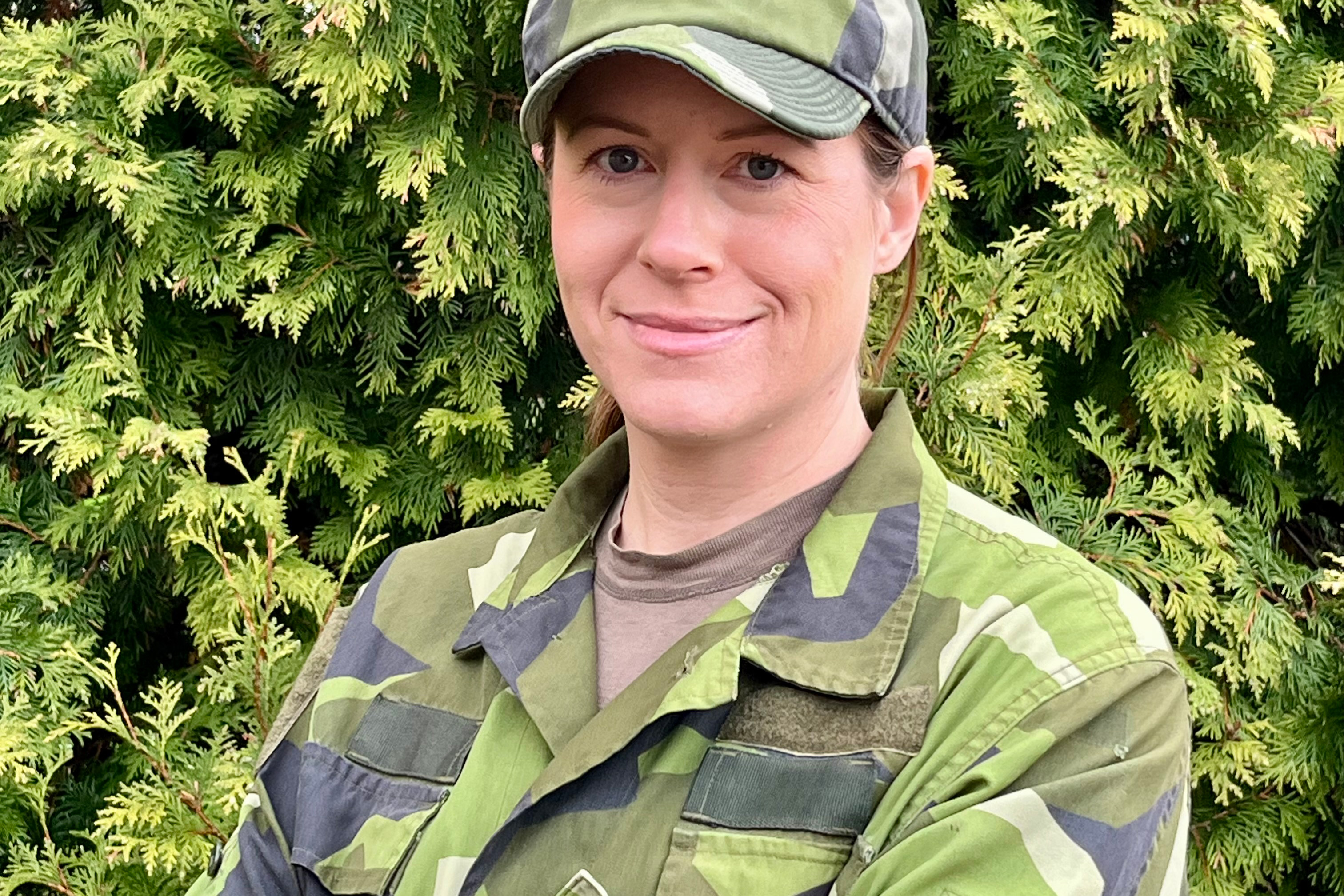en kvinna i militär uniform står framför ett barrträd