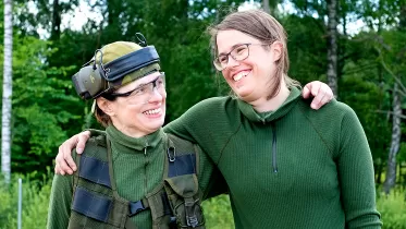Två kvinnor i grönkläder som håller armarna om varandras axlar