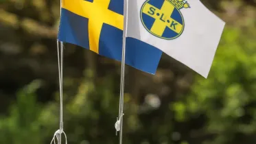 Bilden visar tv flaggor. En svenska flagga och en SLK flagga.